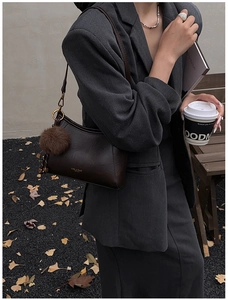 Detail of a dark brown leather underarm bag with a decorative faux fur pom-pom charm