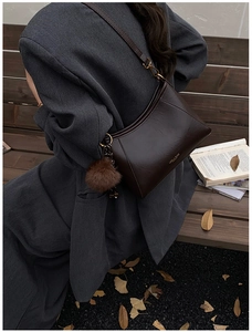 Detail of dark brown leather crossbody bag with pompom charm on a vintage autumn park bench
