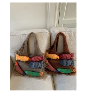 Detail of large knit tote bags with 3D colorful fish charms and long fringe trim on a sofa