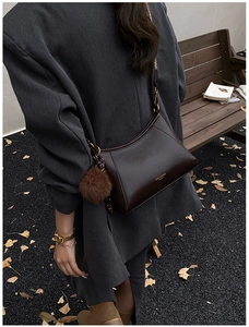 Detail of dark brown leather crossbody bag with fuzzy pom-pom and patterned strap on street