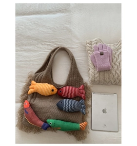 Detailed close-up of brown knit tote bag with colorful fish plush charms and winter gloves