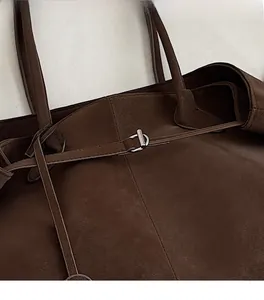 Detail of dark brown suede tote bag featuring a polished metal buckle and fine stitching