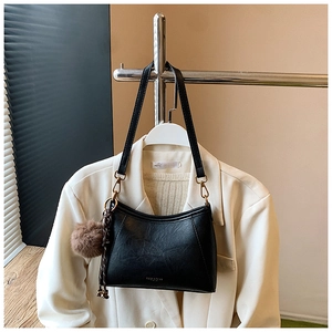 Detail of black glossy leather crossbody bag with gold hardware and plush charm pendant