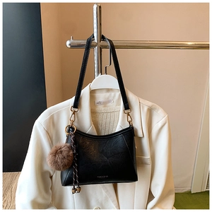 Detail of black faux leather crossbody bag with a brown plush ball charm accessory