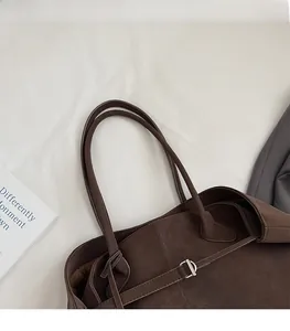 Detail of dark brown suede tote bag featuring slim handles and side metal buckle accents