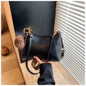 Detail of black crossbody bag with ethnic jacquard strap and plush ball charm accessory