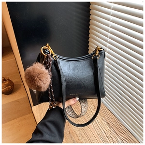 Detail of black retro bucket bag with colorful woven strap and plush ball charm