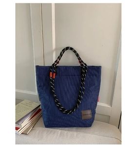 Dettaglio della borsa tote a quadretti blu con manico in corda e toppa logo in pelle