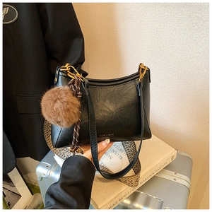 Close-up of black leather dumpling bag with bohemian strap and brown plush charm accessory