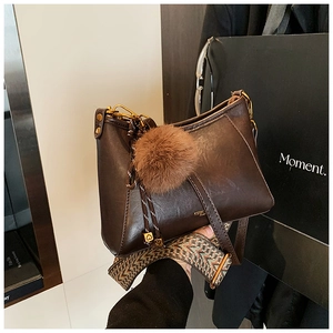 Detail of dark brown dumpling bag with ethnic woven strap and fuzzy ball charm
