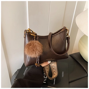 Detail of dark brown dumpling bag with golden logo, faux fur pompom and woven strap