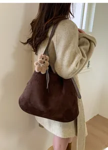 Detail view of large dark brown suede tote bag with cute plush bear charm on soft wool coat