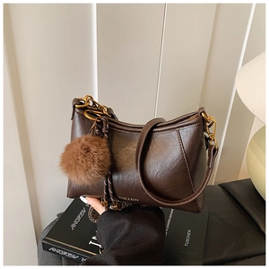 Detail of a brown leather shoulder bag featuring a fuzzy pom-pom charm and gold chain