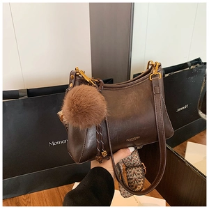 Detail of dark brown leather crossbody bag with fuzzy pompom and patterned strap