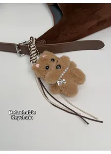 Detail of plush dog bag charm with pearl necklace and woven strap on a brown suede tote