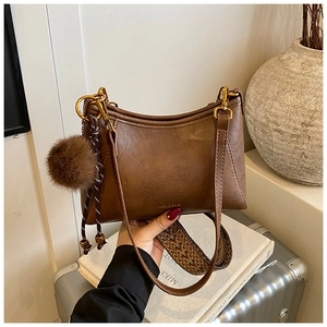 Detail of brown matte leather crossbody bag with ethnic woven strap and fuzzy ball charm