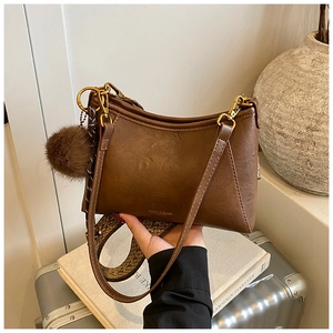 Detail view of brown dumpling bag with patterned woven strap and plush charm accent