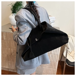 Detail of minimalist black large tote bag with silver metal lock on a gray suit model