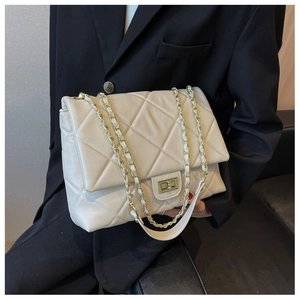 Macro shot of cream quilted shoulder bag with gold chain strap and turn-lock closure