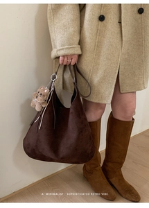 Detail of deep brown suede hobo bag with twisted handle and plush bear charm accent
