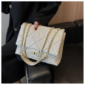 Close-up of cream quilted flap bag with gold chain strap and turn-lock on black suit