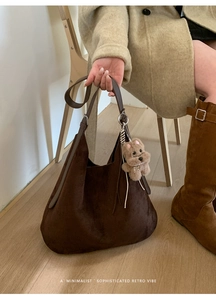 Detail of a brown suede large tote bag with a cute plush dog charm and leather strap