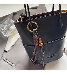 Close-up of black leather handbag with brown woven rope and wooden bead tassel detail