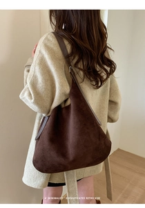 Deep brown minimalist suede hobo bag with adjustable strap worn by a model in a studio