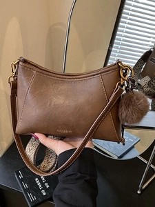 Vintage brown crossbody dumpling bag with patterned wide strap and plush ball charm