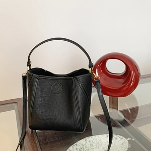 Detail of black pebbled leather bucket bag with gold hardware on glass tabletop