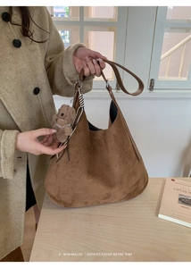 Detail of soft brown suede tote bag with a cute plush bear pendant on wooden background