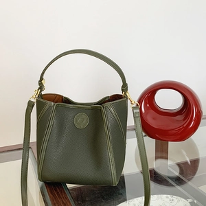 Macro detail of dark green pebbled leather texture and embossed logo on the bucket bag