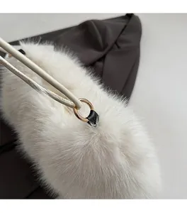 Detail of white faux fur handbag featuring gold round metal ring and cream leather strap