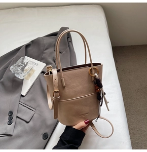 Detail of beige leather bucket bag with top handle, crossbody strap and tassel accessory