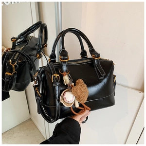 Detail showing shiny black Boston handbag with golden hardware and plush bear charm