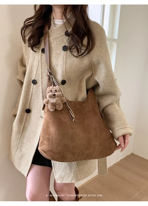 Brown suede half-moon shoulder bag with plush dog charm styled on a wool coat