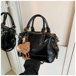 Detail of black glossy leather Boston bag with white stitching and brown bear charm