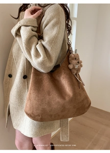 Side view of brown suede hobo bag with teddy bear charm on model's shoulder