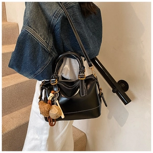 Detail of black Boston leather tote with gold hardware and plush charms on a model