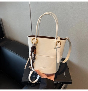 Close-up of white leather bucket bag with gold hardware and tassel charm on books