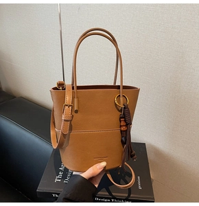 Close-up of brown leather bucket bag featuring fringe pendant and fashion logo text
