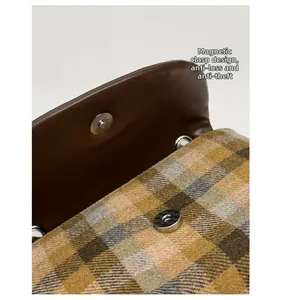 Detail of the magnetic buckle closure on a brown checkered plaid flap saddle bag