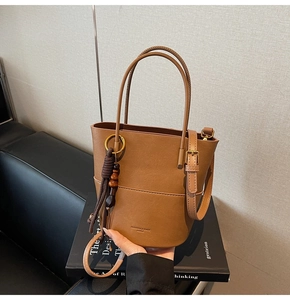 Close-up of brown faux leather bucket bag with wooden bead tassel and fashion branding