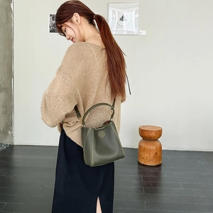 Deep green bucket bag in pebble leather worn as a crossbody in a modern art gallery