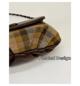 Detail of the pleated design on a brown plaid saddle bag with metal chain strap