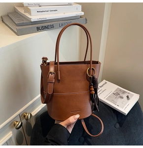 Detail of caramel PU leather bucket bag with beaded tassel charm and stitch detail