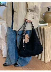 Close-up of black suede hobo bag with brown bear charm and leather tassel detail