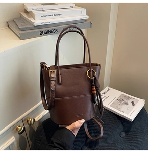 Detail of a brown leather bucket bag featuring wooden bead tassel and slim handles