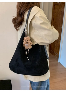 Detail of black suede tote bag with minimalist wide strap and brown teddy bear charm