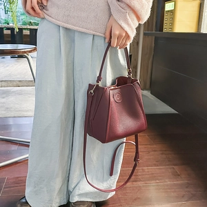 Close-up of a burgundy leather bucket bag with litchi grain and embossed logo detail